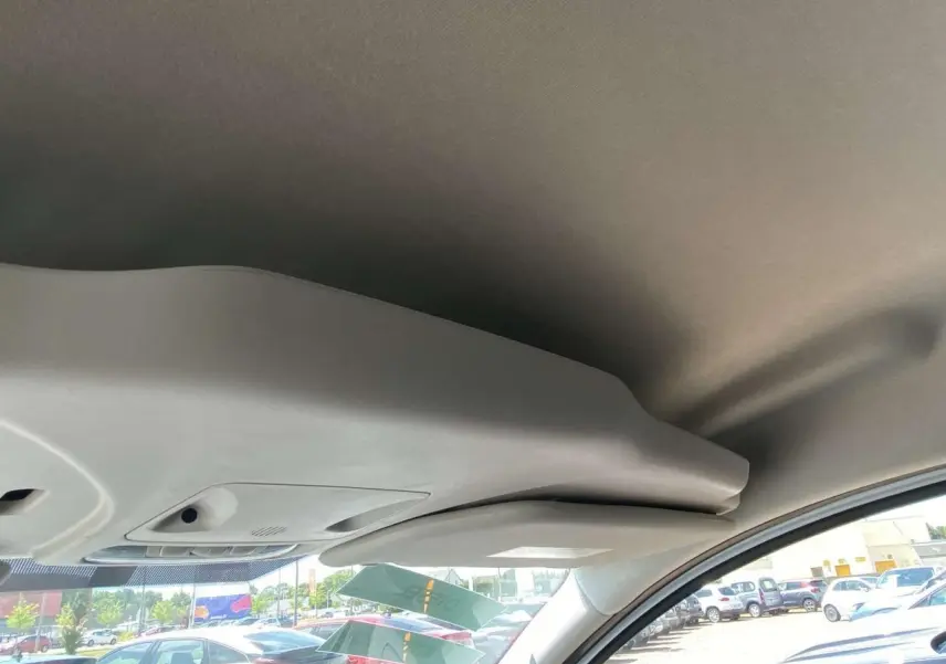 Vue intérieure du toit et pare-soleil côté conducteur d'un Ford Tourneo Courier blanc, avec vue partielle sur le pare-brise et le parking extérieur.