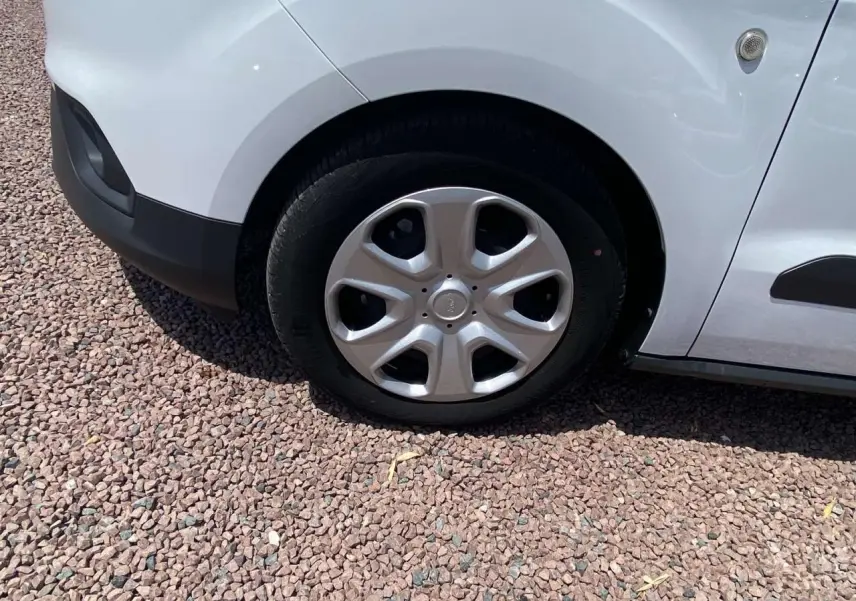 Gros plan sur la roue avant droite avec enjoliveur argenté du Ford Tourneo Courier blanc, sur sol en gravier.