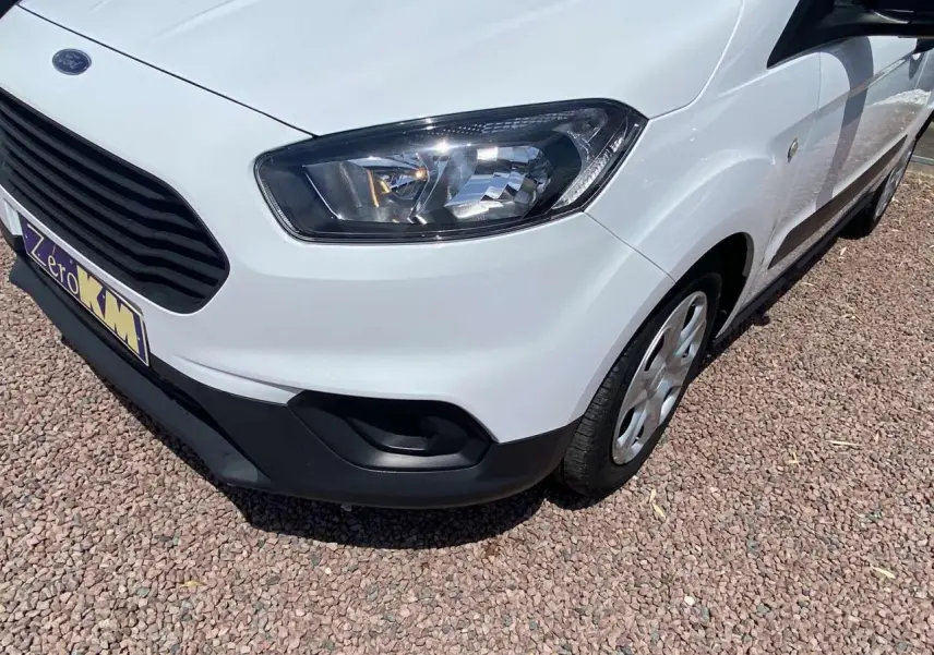 Vue 3/4 avant droit d'un Ford Tourneo Courier blanc avec enjoliveurs cache moyeu sur sol gravillonné.