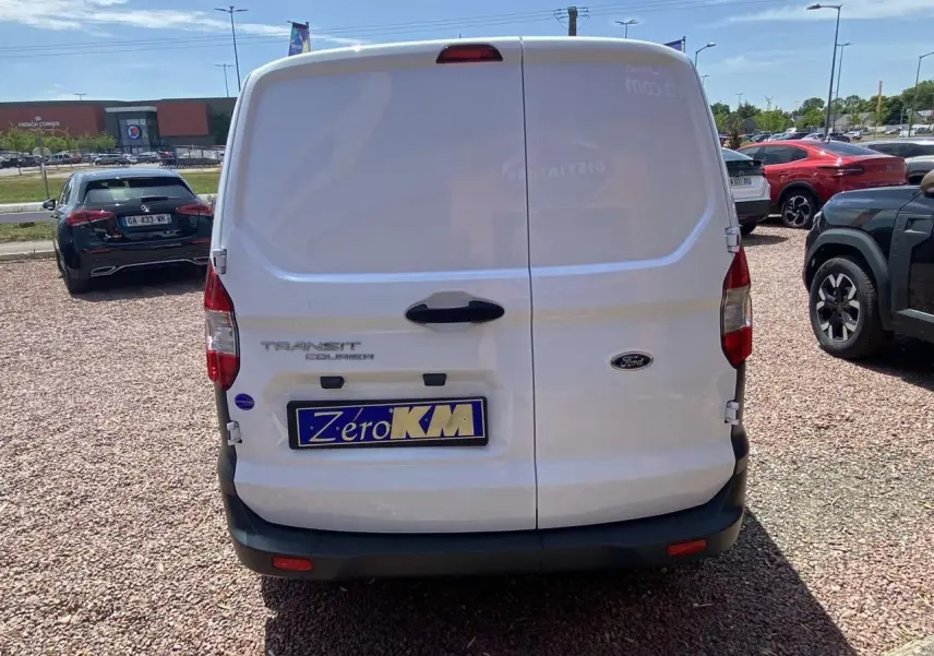 Vue arrière d’un fourgon blanc Ford Tourneo Courier 2022 avec portes battantes tôlées et plaque « Zéro KM » visible.