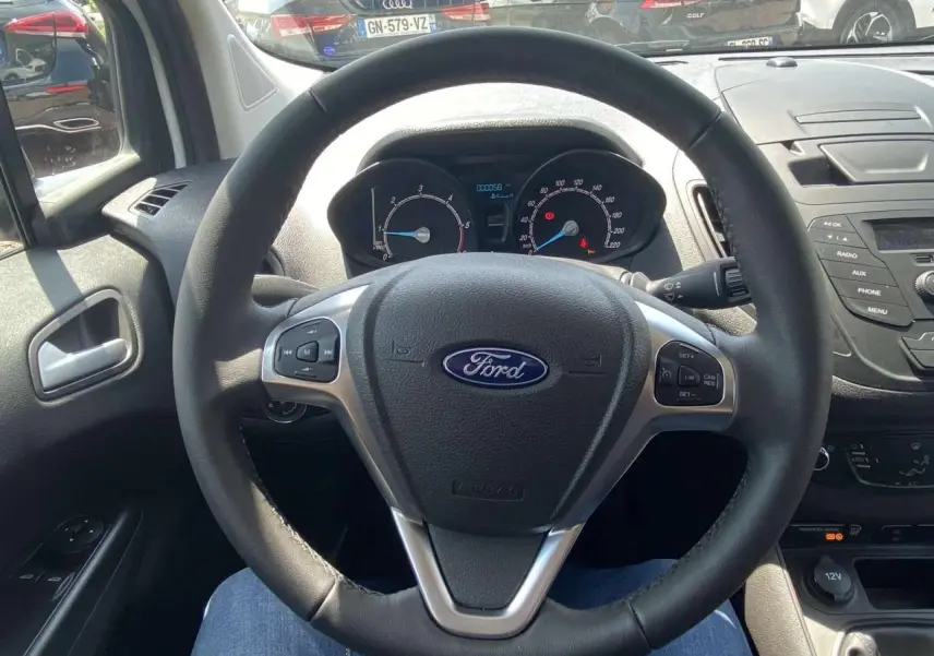 Vue intérieure centrée sur le volant cuir et le tableau de bord du Ford Tourneo Courier blanc, avec commandes au volant visibles.
