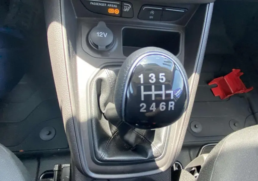 Gros plan sur le pommeau de levier de vitesses manuel noir du Ford Tourneo Courier blanc, avec prise 12V en arrière-plan.