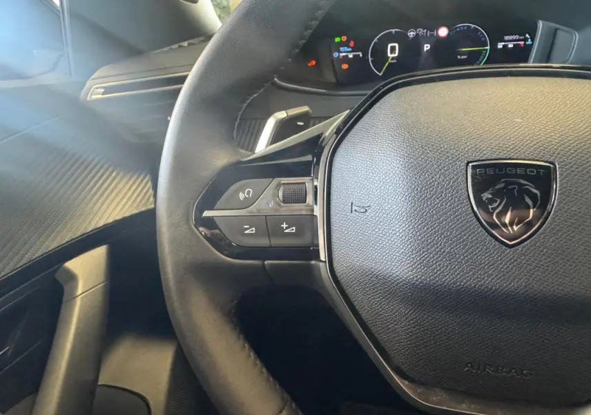Vue rapprochée du volant cuir noir avec logo Peugeot et tableau de bord numérique allumé du 2008 Hybrid 145 Allure.
