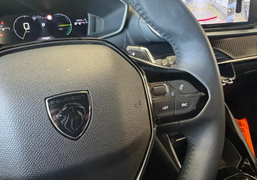 Gros plan sur le volant cuir noir du Peugeot 2008 Hybrid 145 Allure 2025 avec commandes intégrées et tableau de bord numérique.