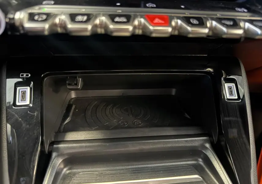 Gros plan sur la console centrale noire du Peugeot 2008 Hybrid 145, avec zone de charge sans fil et ports USB-C.