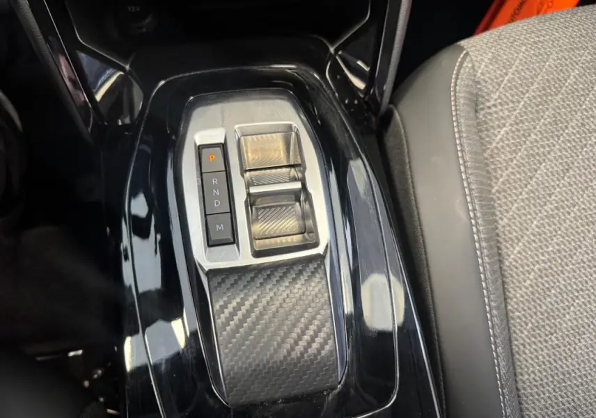 Gros plan sur la console centrale noire brillante avec commandes de boîte auto et accoudoir tissu gris du Peugeot 2008 Hybrid 145.