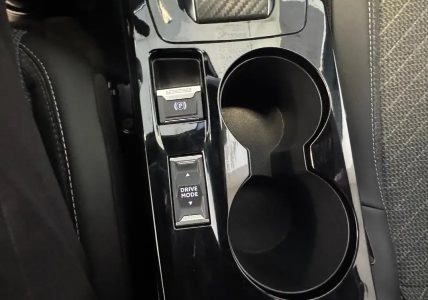 Gros plan sur la console centrale noire du Peugeot 2008 Hybrid 145 Allure, avec boutons frein à main et mode de conduite.