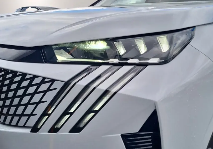 Gros plan sur le phare avant droit blanc du Peugeot 3008 1.2 hybrid 145 GT avec signature lumineuse en griffes LED.