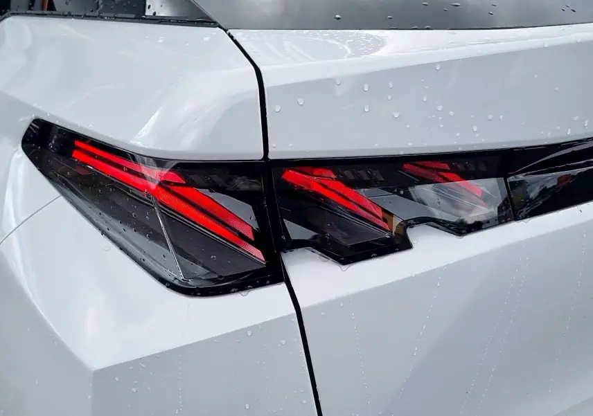 Gros plan sur les feux arrière LED rouges du Peugeot 3008 blanc avec toit noir, vue arrière côté gauche sous la pluie.