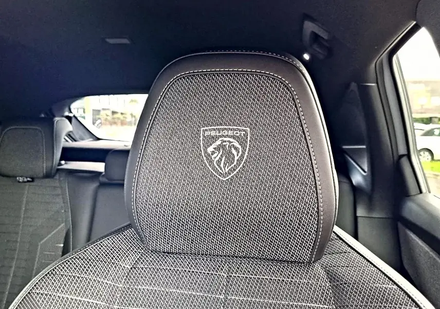 Gros plan sur l'appui-tête avant noir avec logo Peugeot, intérieur tissu et cuir du SUV 3008 blanc toit noir.