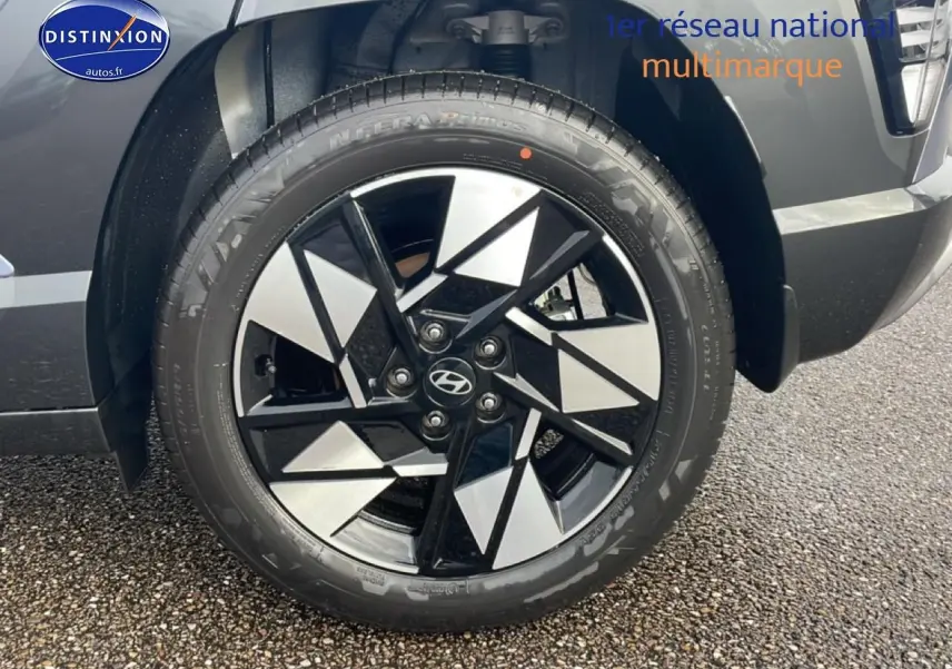 Gros plan sur la roue avant droite avec jante alliage noire et argentée du Hyundai Kona bleu 2025.