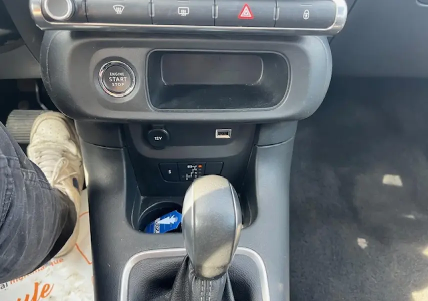 Vue intérieure centrée sur la console centrale d'une Citroën C3 noire 2023, avec levier de boîte auto et bouton start/stop visible.