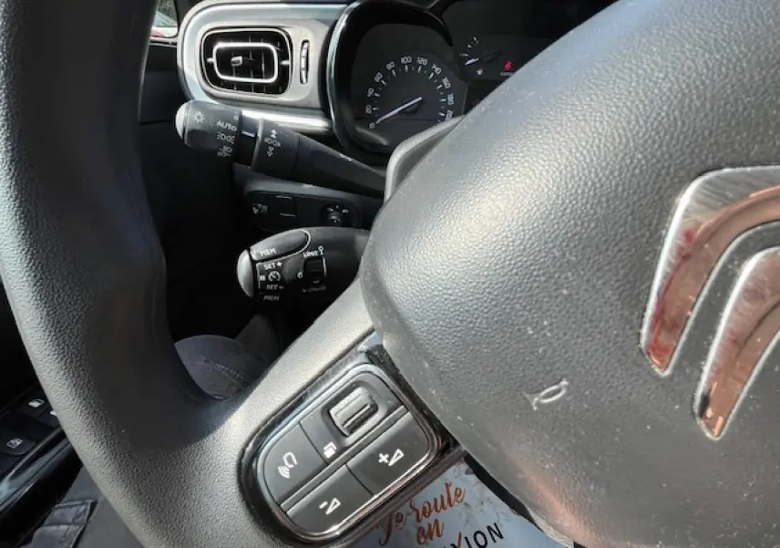 Gros plan sur le volant noir de la Citroën C3 2023 avec commandes audio et tableau de bord en arrière-plan.