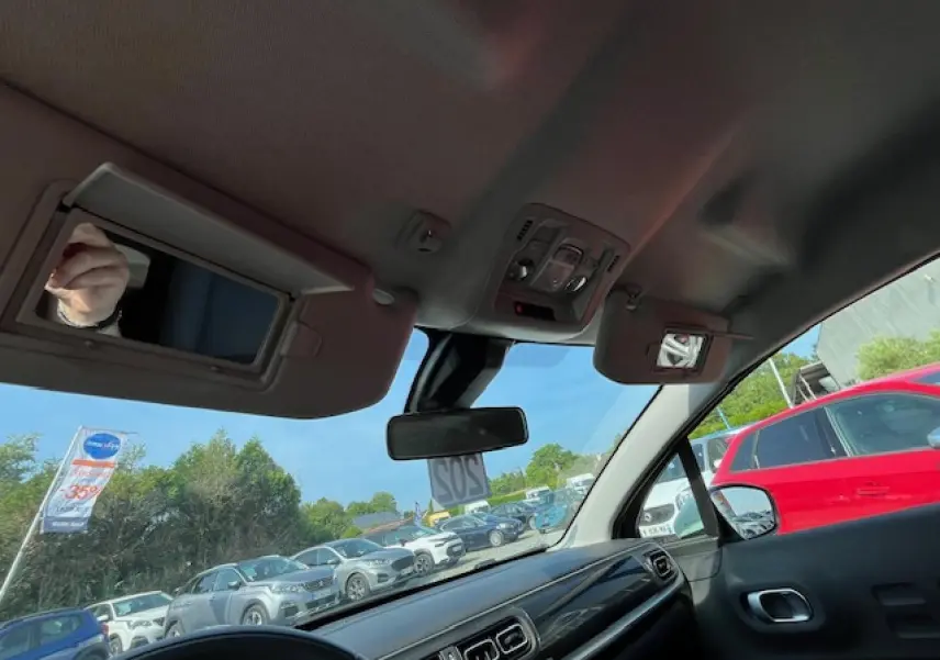 Vue intérieure avant droite du tableau de bord et pare-brise d'une Citroën C3 noire 2023 avec pare-soleil et rétroviseur central.