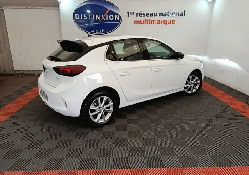 Opel Corsa blanche vue 3/4 arrière droit en intérieur, avec jantes alliage et toit avec spoiler noir.