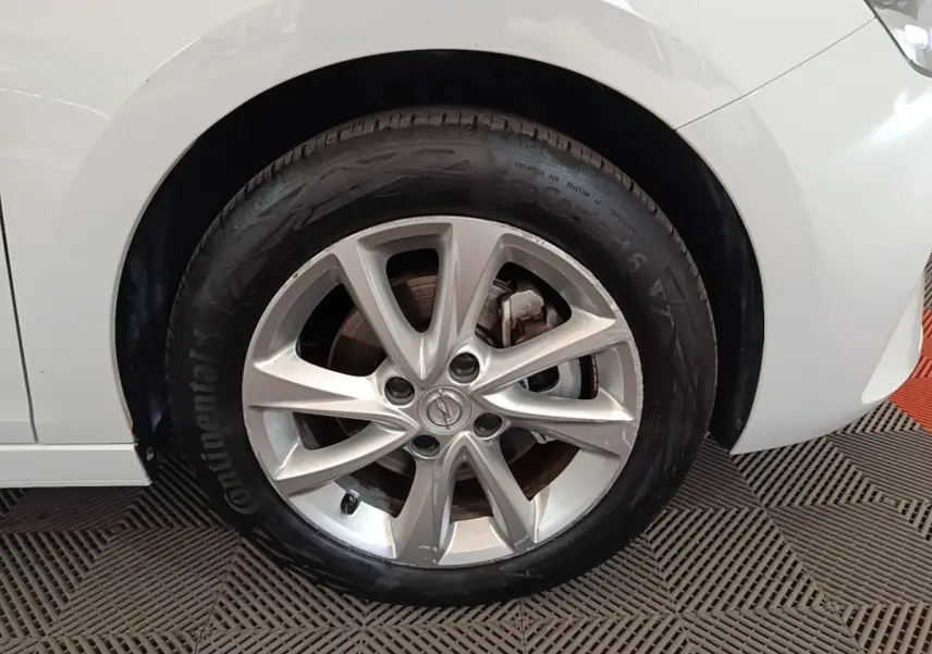 Gros plan sur la roue avant droite d’une Opel Corsa blanche 2022 avec jante alliage et logo Opel visible.