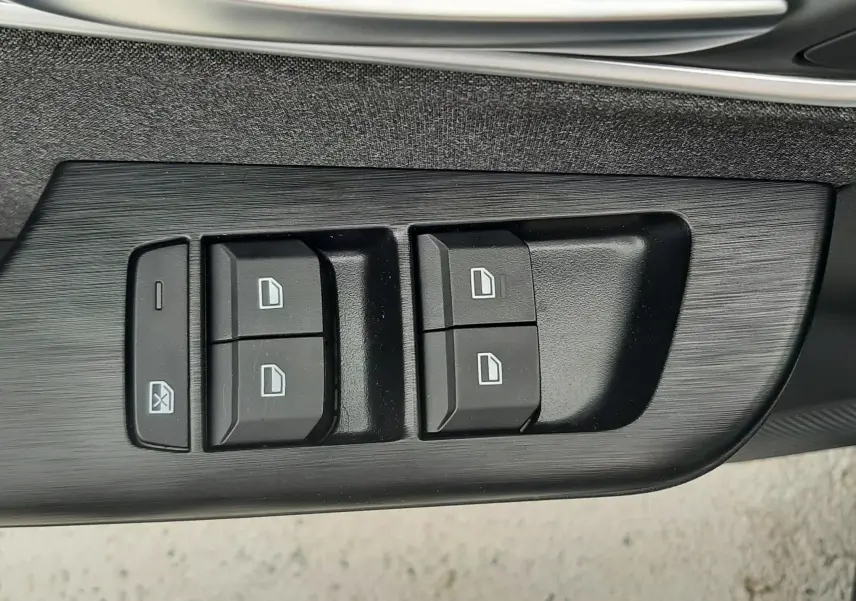 Gros plan sur les commandes de lève-vitres noires intégrées dans la porte intérieure du MG MOTOR ZS Camden Grey.