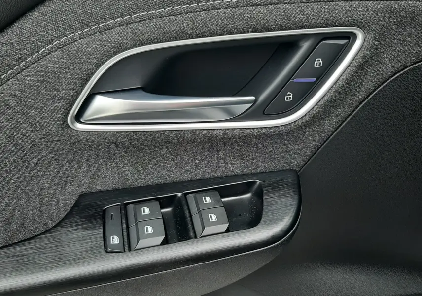 Gros plan sur la poignée intérieure et les commandes de fenêtre côté conducteur du MG ZS Camden Grey, finition tissu et plastique noir.