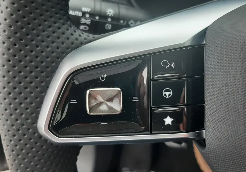 Gros plan sur les commandes gauche du volant perforé noir du MG ZS Camden Grey 2026, avec boutons multifonctions et finition argentée.
