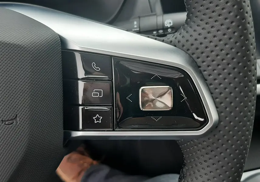 Gros plan sur les commandes multifonctions à gauche du volant perforé noir du MG MOTOR ZS Camden Grey 2026 hybride.
