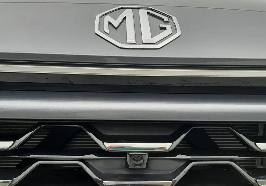 Gros plan sur la calandre avant grise Camden Grey du MG ZS 1.5 Hybrid+ avec logo MG et caméra frontale intégrée.