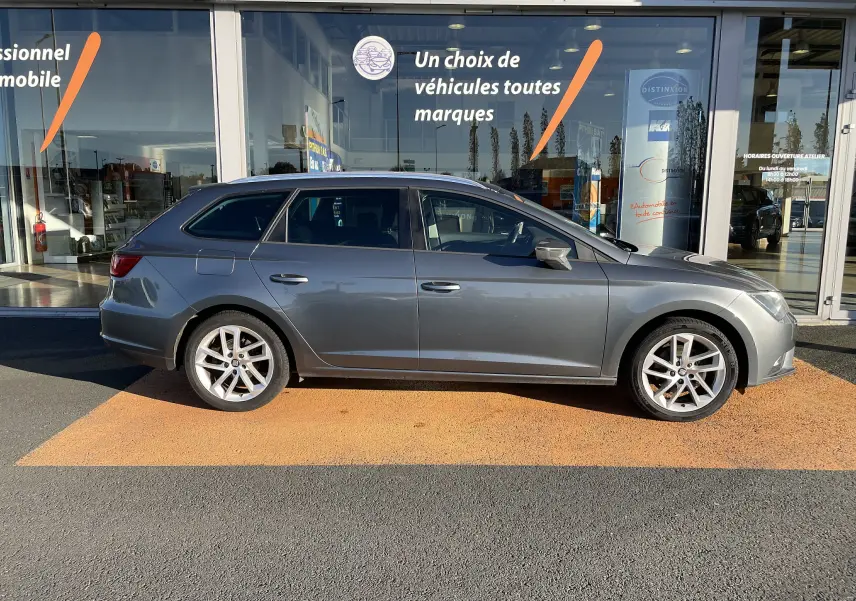 Profil côté gauche d'une SEAT LEON ST gris 2013 avec jantes alliage et vitres teintées, stationnée devant un showroom.