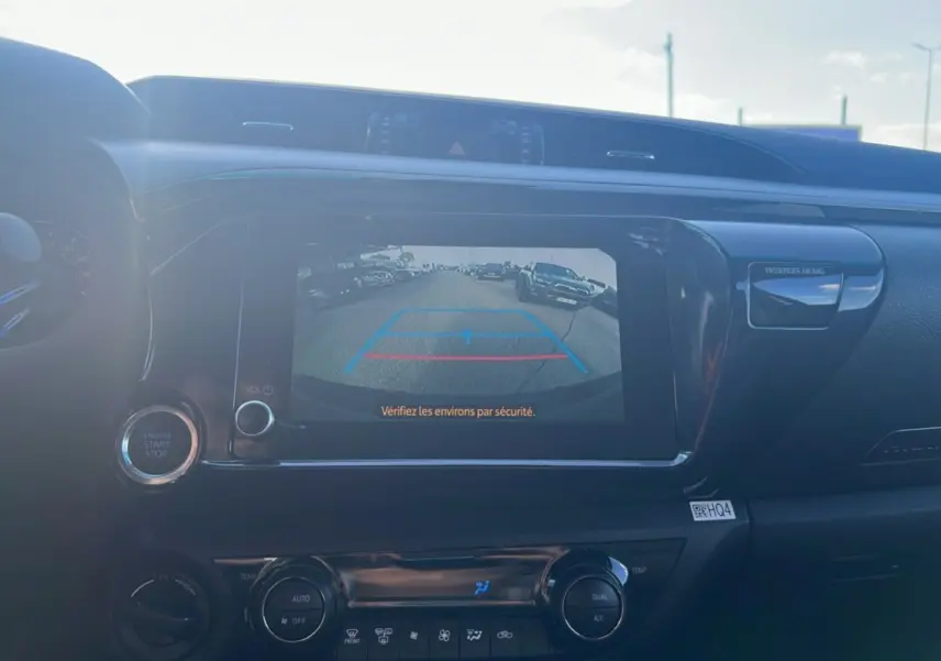 Vue intérieure du tableau de bord du Toyota Hilux 2025 gris atlas, écran affichant la caméra de recul avec consigne de sécurité.