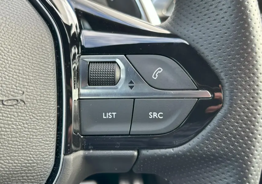 Gros plan sur les commandes gauche du volant cuir perforé du Peugeot 3008 2024, boutons noirs et chrome brillant.