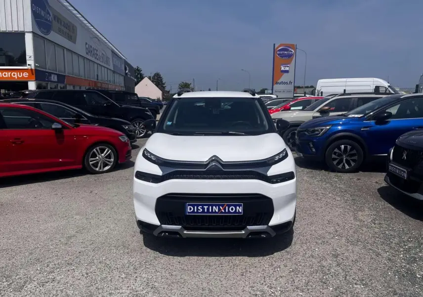 Vue avant d'un Citroën C3 Aircross blanc banquise avec calandre noire et barres de toit noires, stationné en extérieur.