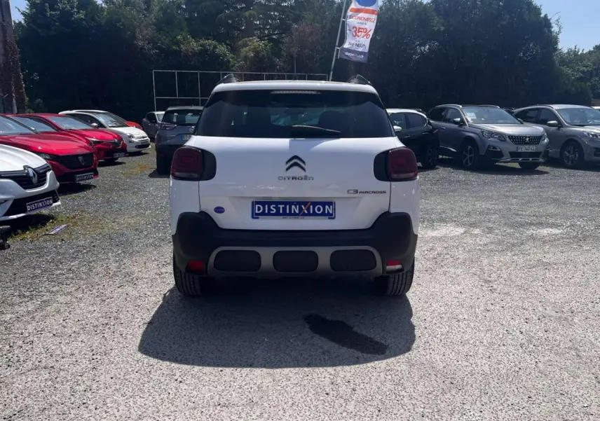 Vue arrière d'un Citroën C3 Aircross blanc banquise avec barres de toit noir brillant sur un parking extérieur.