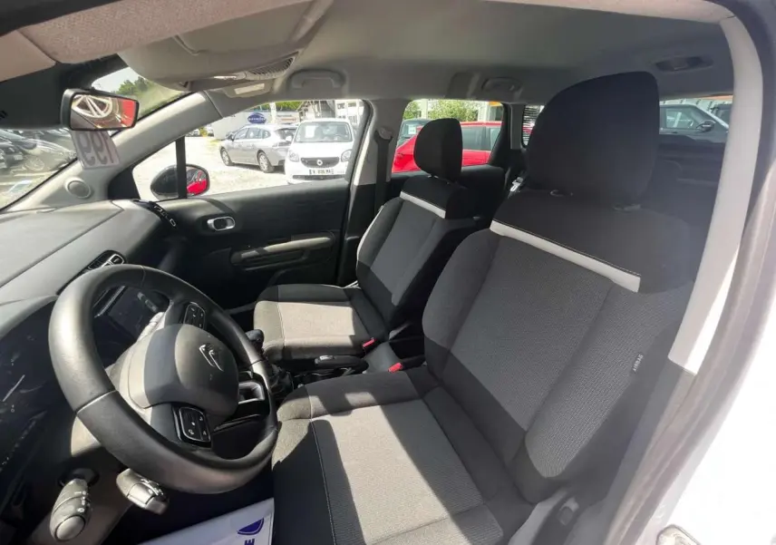 Intérieur avant du Citroën C3 Aircross blanc banquise 2023, sièges tissu gris et volant multifonction noir.