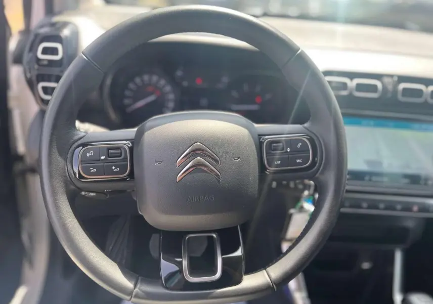 Vue rapprochée du volant noir de la Citroën C3 Aircross 2023 avec commandes intégrées et tableau de bord flou en arrière-plan.