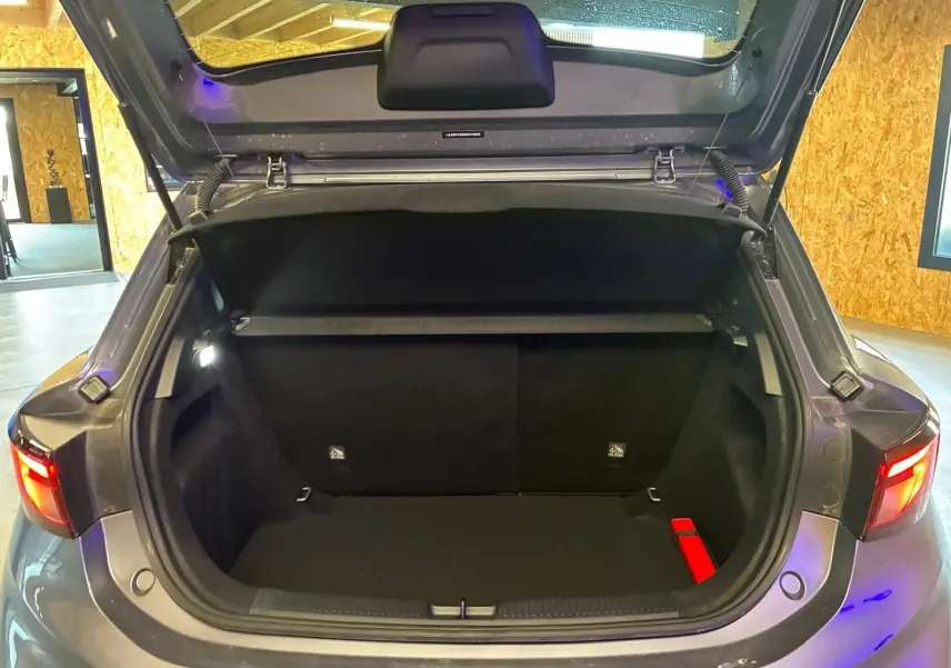 Coffre ouvert d'une MG3 1.5 HYBRID+ noire, vue arrière, avec feux arrière allumés dans un garage.