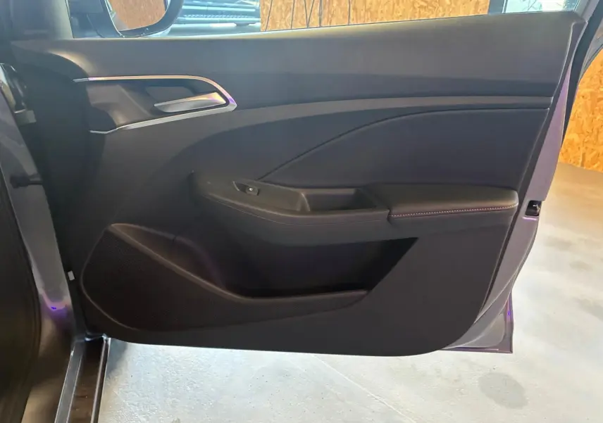Vue intérieure de la porte avant gauche noire du MG3 1.5 HYBRID+ 195 LUXURY avec poignée argentée et accoudoir rembourré.
