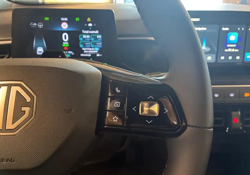 Gros plan sur le volant noir du MG3 1.5 HYBRID+ 195 LUXURY avec commandes intégrées et tableau de bord digital en arrière-plan.