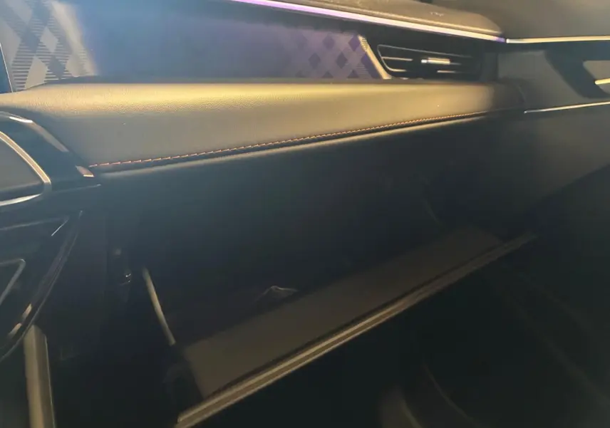 Intérieur de la MG3 1.5 HYBRID+ 195 LUXURY noir, vue côté passager sur la boîte à gants ouverte et tableau de bord cuir.