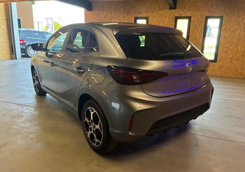Vue 3/4 arrière droite d'une MG3 1.5 HYBRID+ 195 Luxury gris métallisé avec jantes noires et toit noir en intérieur showroom.