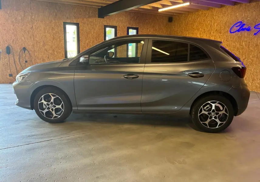 Vue latérale droite du MG3 1.5 HYBRID+ 195 LUXURY gris métallisé avec jantes alliage et vitres teintées en intérieur showroom.