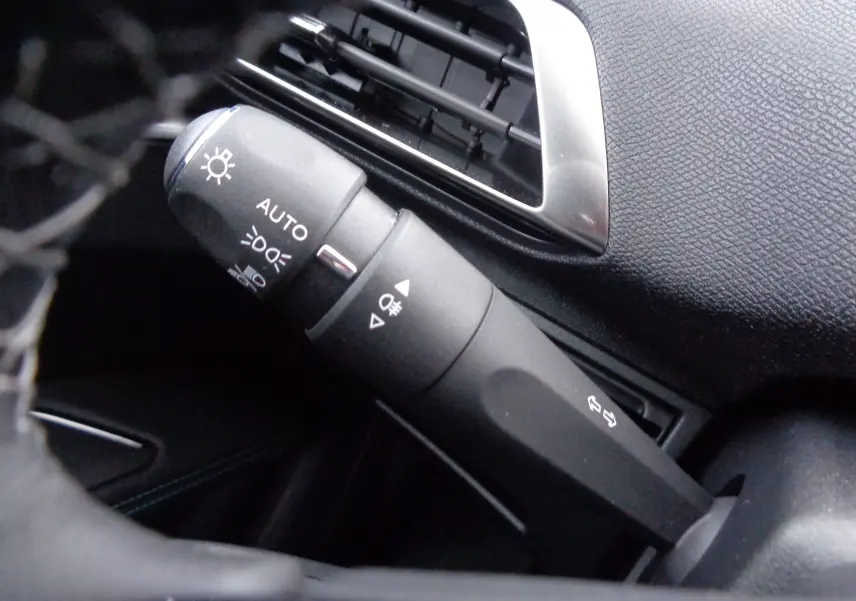 Gros plan sur la commande des phares et clignotants du Peugeot 3008 noir Perla Nera, avec sortie d'air chromée visible.