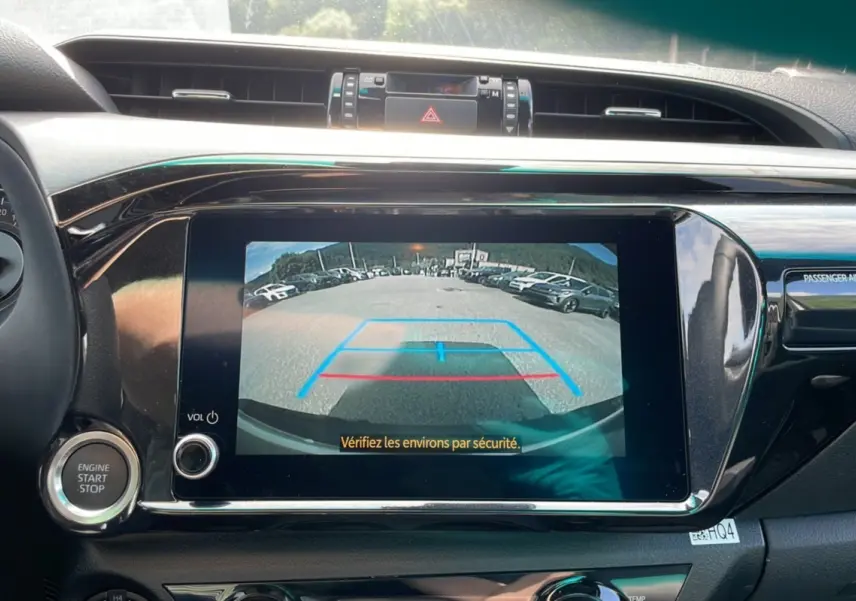 Vue intérieure du tableau de bord du Toyota Hilux 2025 blanc, écran multimédia affichant la caméra de recul avec repères colorés.