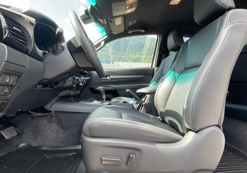 Intérieur du Toyota Hilux 2025 X-TRA D-4D 204 BVA Invincible, vue côté conducteur sur sièges cuir gris et tableau de bord.