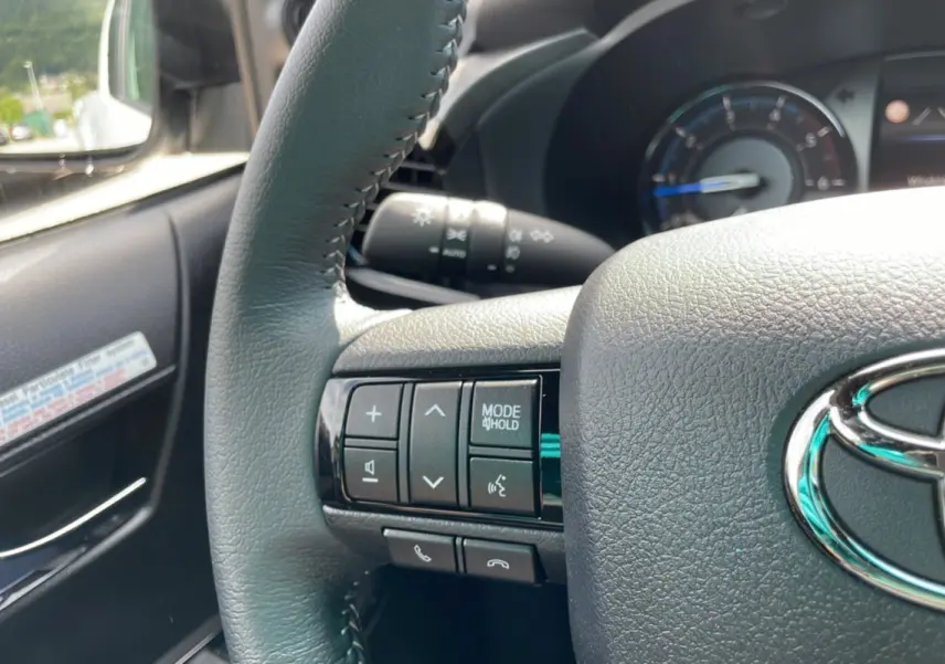 Gros plan sur le volant côté gauche du Toyota Hilux 2025 blanc, avec commandes multimédia et logo Toyota visible.
