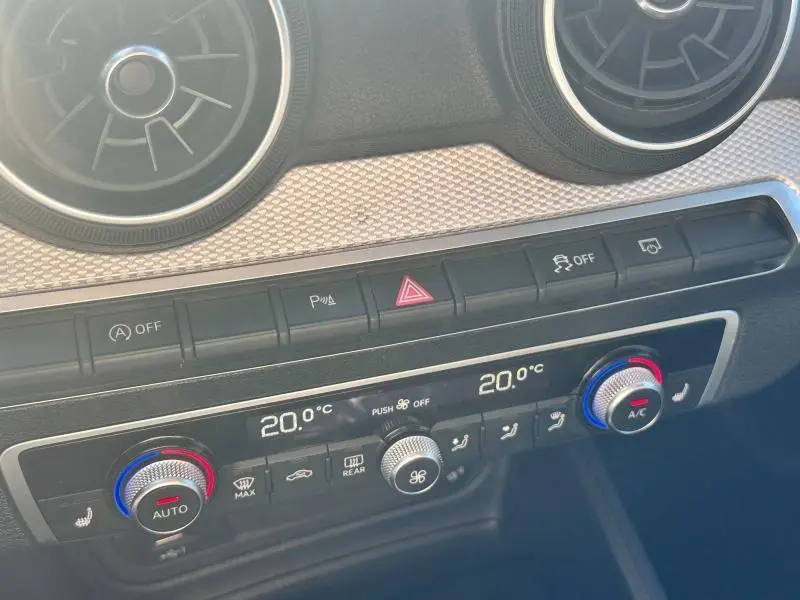 Détail du tableau de bord de l'Audi Q2 35 TFSI 2023, montrant la climatisation digitale et les aérateurs ronds chromés.