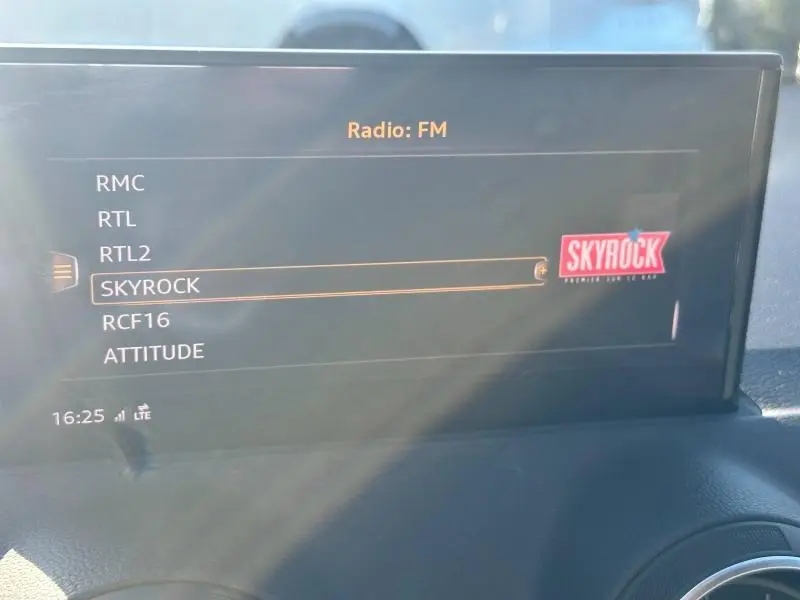 Écran central de l'Audi Q2 2023 affichant la liste des radios FM, avec sélection sur Skyrock, intérieur en lumière naturelle.