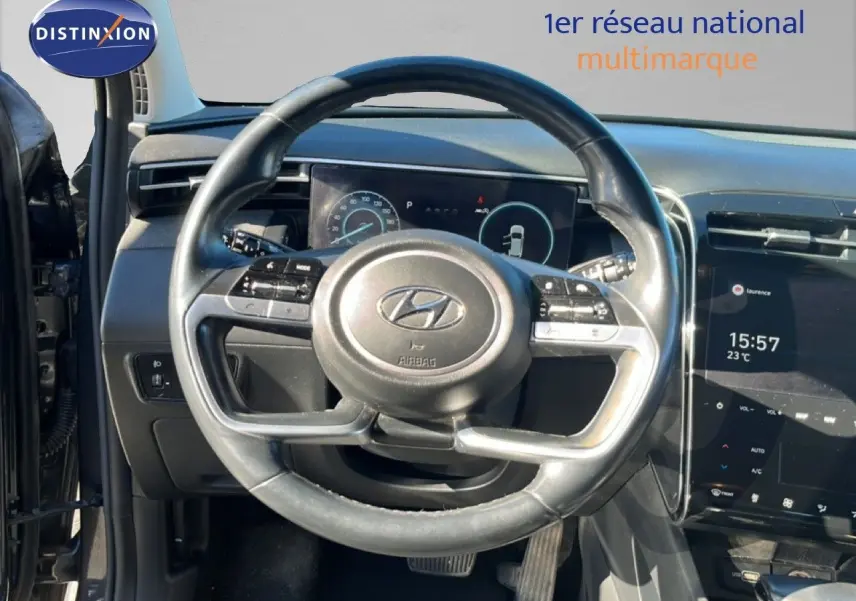 Vue intérieure centrée sur le volant du Hyundai Tucson gris foncé, avec tableau de bord numérique et écran tactile visible.