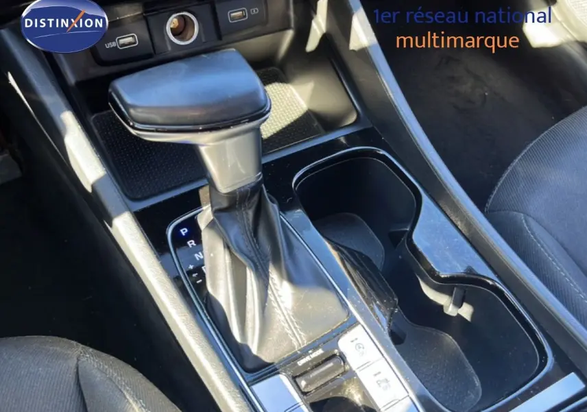 Gros plan sur le levier de vitesses automatique du Hyundai Tucson gris foncé, avec porte-gobelets et prises USB visibles.