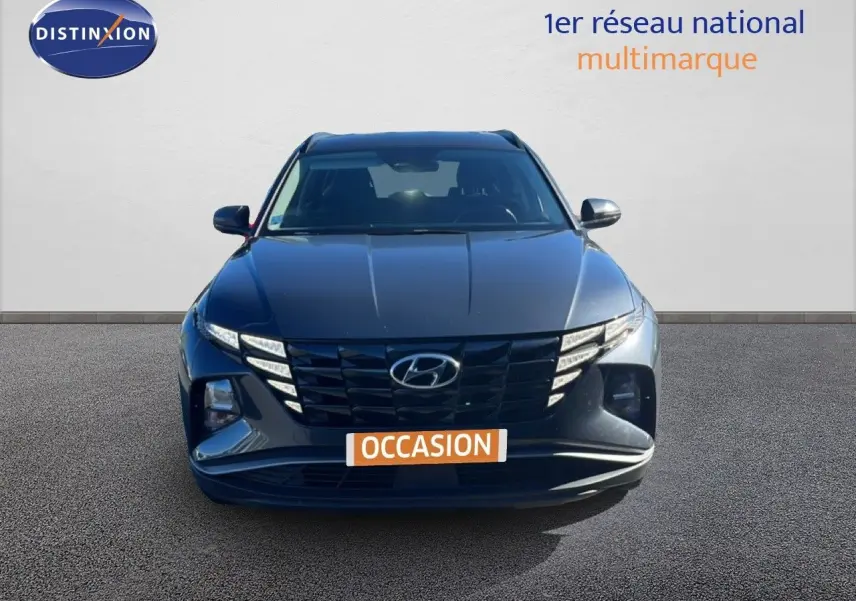 Vue avant d’un Hyundai Tucson gris foncé métal, avec calandre noire et feux LED distinctifs allumés.