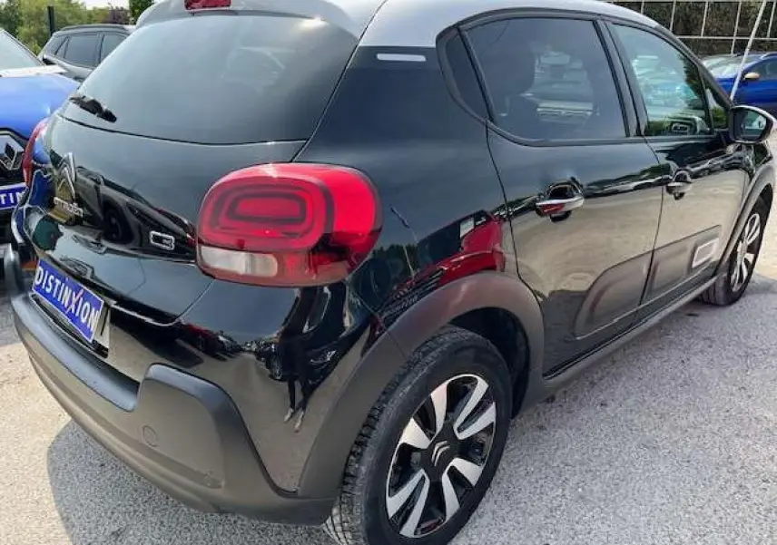 Vue 3/4 arrière droite d'une Citroën C3 noire avec toit blanc, jantes alliage diamantées et vitres surteintées.