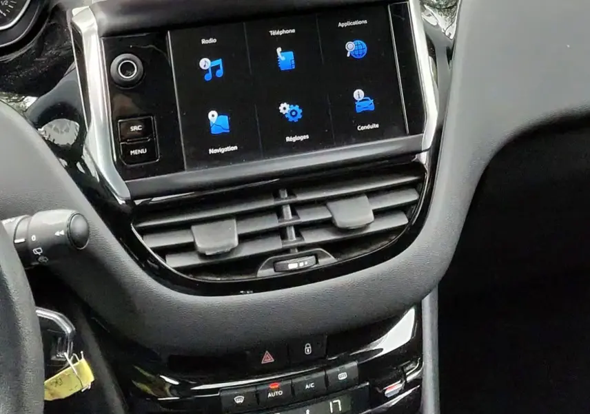 Vue intérieure du tableau de bord de la Peugeot 208 gris foncé, avec écran tactile et levier de vitesse manuel visible.