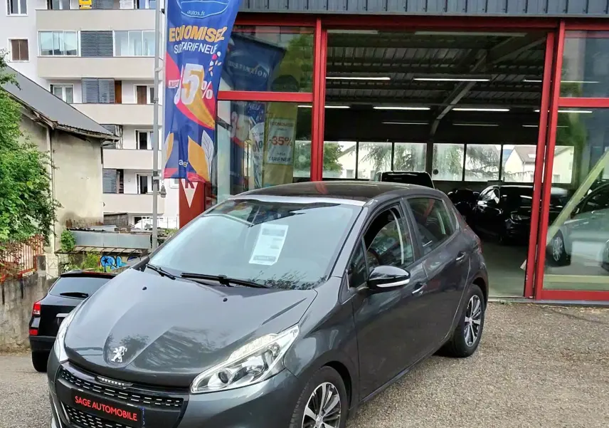 Peugeot 208 gris foncé métal vue 3/4 avant droit devant un garage avec enseigne AD Expert.